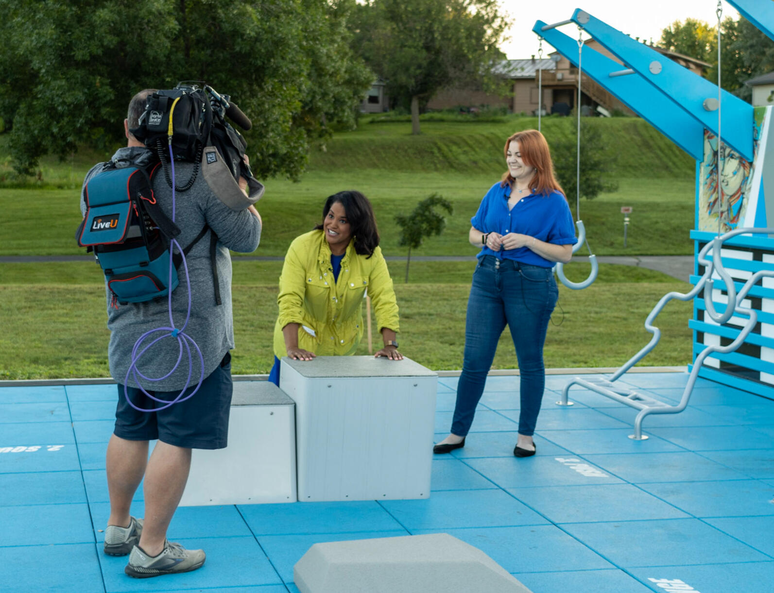 Two women being filmed for a TV show on an outdoor fitness court